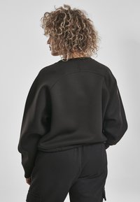 Felpa nera oversize con scollatura tonda e maniche raglan, realizzata in tessuto morbido. Presenta una superficie liscia e una vestibilità comoda, abbinata a pantaloni coordinati.