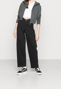 Sudadera gris corta con cremallera frontal combinada con pantalones anchos negros y zapatillas bajas en blanco y negro.