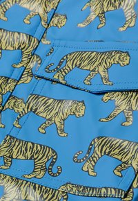 Modra tkanina z ponovljenim vzorcem tigra v rumeni in črni barvi. Material ima sijajen zaključek z našitimi detajli in žepi.