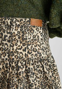 Spijkerrok met luipaardpatroon, voorzien van een uitlopende vorm, een lichtbruine tailleband met een leren label en een gestructureerde stof. Kleuren zijn bruin, zwart en beige.