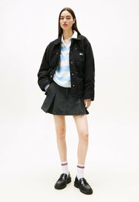 Chaqueta acolchada negra, polo a rayas azul y blanco, falda de denim oscura, mocasines negros, calcetines blancos con rayas rojas y negras. Diseño minimalista.