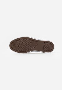 Semelle en caoutchouc d'une basket Converse marron avec motifs de crampons en losange et en ligne, semelle intermédiaire blanche, vue du dessous sur fond blanc uni.