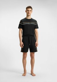 Zwarte T-shirt met korte mouwen, voorzien van witte en gouden strepen op de borst, gecombineerd met zwarte shorts met gouden zijaccenten en een trekkoord.