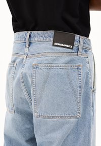 Jean en denim bleu clair avec une coupe décontractée, doté d'une étiquette en tissu noir avec "ARMEDANGELS" à la taille et de détails cousus sur les poches.