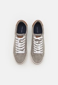 Hallid hallid kanvas sneakersid valgete nööridega, pruun nahkne aktsent kandadel ja tumbluust siseruum, millel on brändi logo.