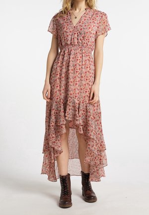 Kobieta w sukience w kwiaty o kroju high-low, z krótkimi rękawami, dekoltem w serek, falbaną na dole oraz brązowych botkach za kostkę z wiązaniem.