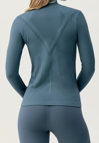 Maglietta sportiva a maniche lunghe in tessuto grigio-blu, con un retro superiore testurizzato, linee di pannello e dettagli a pois lungo la parte bassa della schiena.