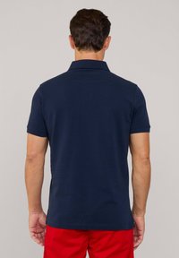 Granatowa koszulka polo wykonana z bawełny, z klasycznym kołnierzykiem, krótki rękaw i prosty dół, przedstawiona od tyłu.