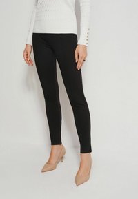 Czarne dopasowane legginsy uszyte z elastycznego materiału. W połączeniu z białym swetrem o fakturze i beżowymi szpilkami.