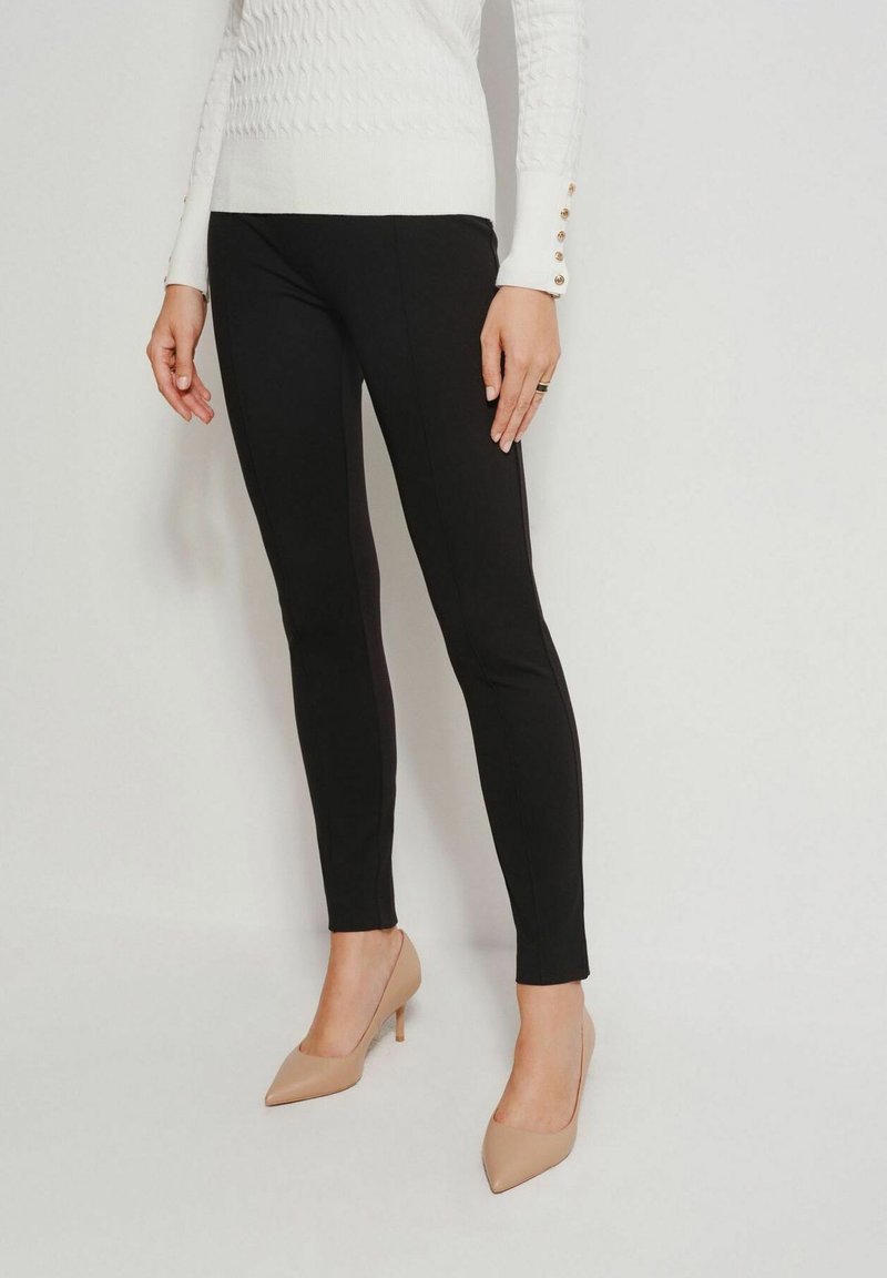 Czarne dopasowane legginsy uszyte z elastycznego materiału. W połączeniu z białym swetrem o fakturze i beżowymi szpilkami.