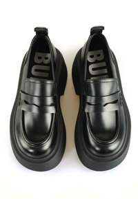 Melni ādas loaferi ar masīvu zoli, ar dekoratīvu siksniņu un gludu apdari. Apaļš purngals un smalki šuvumu raksti.