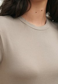 Beige ribbet t-shirt med rund hals, lavet af et tekstureret stof og diskrete vertikale linjer. Let tætsiddende, enkelt design.