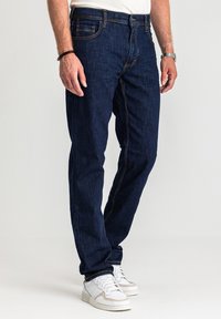 Granatowe dżinsy o prostym kroju, z pomarańczowymi przeszyciami, pięcioma kieszeniami i podwyższonym stanem. Do tego białe trampki.