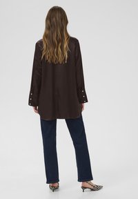 Brown satin long-sleeve shirt with buttoned cuffs, paired with dark blue straight-leg jeans and black and white patterned heeled shoes.