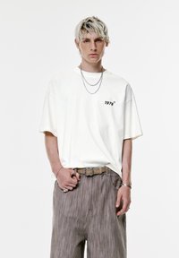 Hvid oversized T-shirt med sort "1978" logo på brystet, parret med lysebrune stribede bukser. Sølv halskæder og et bælte fremhæver outfittet.
