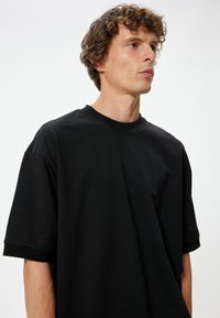 Czarny bawełniany t-shirt z krótkim rękawem, posiadający okrągły dekolt i luźny krój. Gładka tekstura, bez widocznych wzorów czy akcentów.