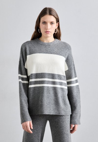 Grå sweater med hvide striber, rund halsudskæring og lange ærmer. Blød struktur; har en afslappet pasform og ribkant. Bæres med grå bukser.