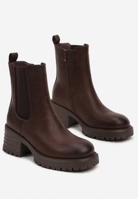 Bottes de cheville en cuir marron avec panneaux latéraux élastiques, bout arrondi et semelle empilée. Elles disposent d'une fermeture éclair sur le côté et d'un dessus texturé.