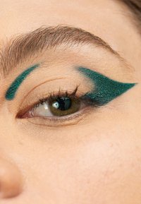 Smaragdfarget eyeliner danner en skarp vinge over et nøytralt øyelokk, som kontrasterer med naturlige vipper og hudtone, og fremhever øyet.