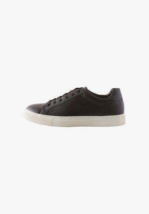 Zapatilla baja de piel texturizada marrón oscuro con cordones negros y suela de goma blanca, vista lateral sobre fondo blanco.