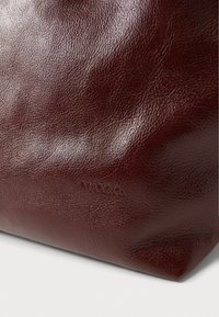 Brązowa torba ze skóry o fakturowanym wykończeniu. Na dole wytłoczono logo "MAX&Co.". Prosty, niestandardowy fason z zaokrąglonymi krawędziami.