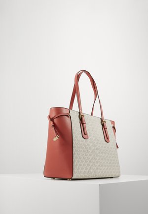 Torba typu tote z bocznymi panelami i uchwytami z brązowej skóry, beżowa tkanina z nadrukiem powtarzającego się wzoru "MK", złote ozdobne elementy, na białym postumencie.