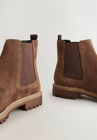 Brown suede chelsea boots with elastic side panels and pull tabs. Features a textured rubber sole with deep treads for grip.
