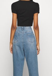 T-shirt noir court avec des manches courtes bouffantes associé à un jean en denim léger taille haute de couleur bleu clair, comportant deux poches arrière et un motif délavé.