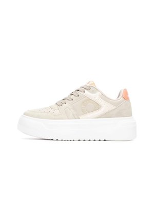 Zapatillas de ante beige con suela gruesa blanca, que presentan perforaciones, cordones beige y una lengüeta en la parte trasera de color naranja. Marca en el lateral.