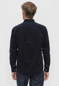 Marinblå kordflodsskjorta med lång ärm, knäppmanschetter och en detalj med veck bak. Slät textur, skräddarsydd passform och klassisk krage.