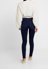 Suéter texturizado crema y jeans skinny azul oscuro. El suéter tiene un exterior esponjoso, mientras que los jeans presentan bolsillos traseros con costuras visibles.