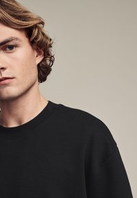 Zwarte sweatshirt met ronde hals, zachte textuur en een comfortabele pasvorm. Zichtbare stiksels bij de kraag en schoudernaden.