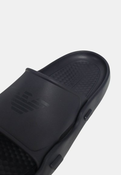 Černé gumové skluzové sandály s texturovanou stélkou, širokým popruhem s jemným logem a hladkým, zakřiveným designem podrážky.