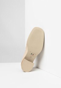 Beżowe skórzane buty o eleganckim designie, z gładką teksturą, zaokrąglonym noskiem i teksturowaną gumową podeszwą. Widoczne oznaczenie marki na spodzie.