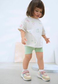Kortærmet hvidstribet skjorte med farverig frugtbroderi, parret med grønne shorts og multikolor sneakers med velcro-stropper.