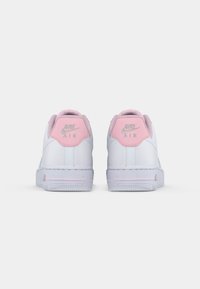 Le sneakers Nike Air presentano una tomaia in pelle bianca con accenti rosa sulla linguetta del tallone e sul colletto, suola in gomma testurizzata e logo ricamato.