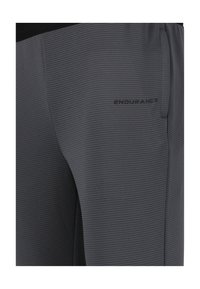 Grau sportliche Hose mit einem strukturierten Rippmuster, ausgestattet mit einem schwarzen Bund und einem kleinen schwarzen Logo an der Seite.