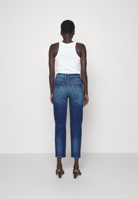 Vaqueros de mezclilla azul oscuro con cintura alta, pierna recta, bolsillos traseros y una textura desgastada. Combinados con una camiseta sin mangas blanca y tacones negros.