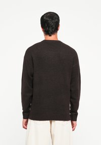 Donkerbruin gebreid sweater met een ronde halslijn, losse fit, geribbelde manchetten en zoom. Gladde textuur, zichtbare naad langs de rug.