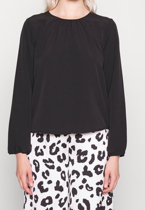 Femme portant un haut noir uni à manches longues associé à un pantalon blanc avec un imprimé léopard noir audacieux.