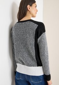 Maglione lavorato a maglia con un motivo testurizzato grigio e nero, con polsini a coste e una fascia bianca in basso, mostrato sulla schiena di un modello.