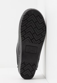 Sorte tresko med teksturert gummisåle som har et zigzag-mønster. Undersiden har merke og størrelse. Glatt skinnoverdel.