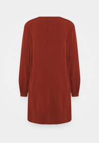 Roestkleurige jurk met lange mouwen, gathered manchet, rechte silhouet en subtiele naaddetails langs de achterkant.