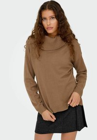 Pull marron à col roulé avec des détails côtelés et des manches longues, associé à une jupe noire texturée. Coupe et silhouette globales décontractées.