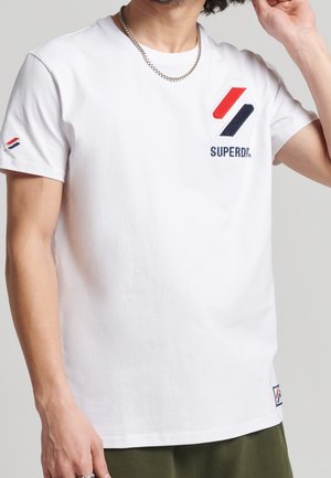 Weißes Baumwoll-T-Shirt mit kurzen Ärmeln, das ein rotes, blaues und weißes Markenlogo sowie Stickerei auf der Brust und an den Ärmelakzenten präsentiert.