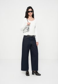 Λευκό μπλουζάκι με ριμπ ύφανση και μακριά μανίκια, σκούρο μπλε τζιν παντελόνι με φαρδιά μπατζάκια και μαύρη ζώνη, διαφανής τσάντα και μαύρα μποτάκια με χοντρό τακούνι.