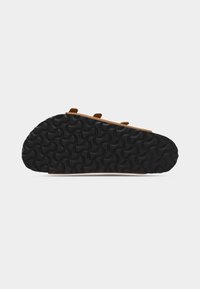 Σόλα καφέ σανδάλου με μαύρο υφασμένο καουτσούκ στο κάτω μέρος που διαθέτει κυρτά, κυματιστά μοτίβα πέλματος, εμφανιζόμενη σε λευκό φόντο.