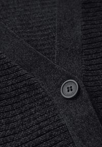 Schwarze Strickjacke mit einem strukturierten Strickmuster und einem glatten, flachen Kragen. Mit einem runden, schwarzen Knopf mit der Aufschrift "Cecil" verziert.