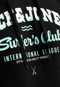 Sudadera negra con texto en blanco y azul claro, que incluye "Surfer's Club" y "International League". El texto incluye olas y iconos cruzados.