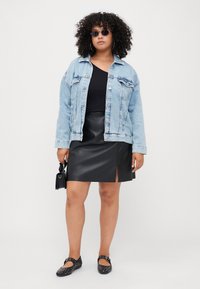 Chaqueta de mezclilla azul claro, top negro ajustado, falda mini de cuero sintético negra con abertura frontal, zapatos planos negros con tachuelas, accessorios con un bolso pequeño.